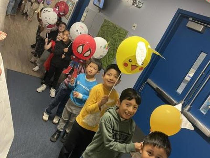Children holding character-themed balloons in a school hallway.