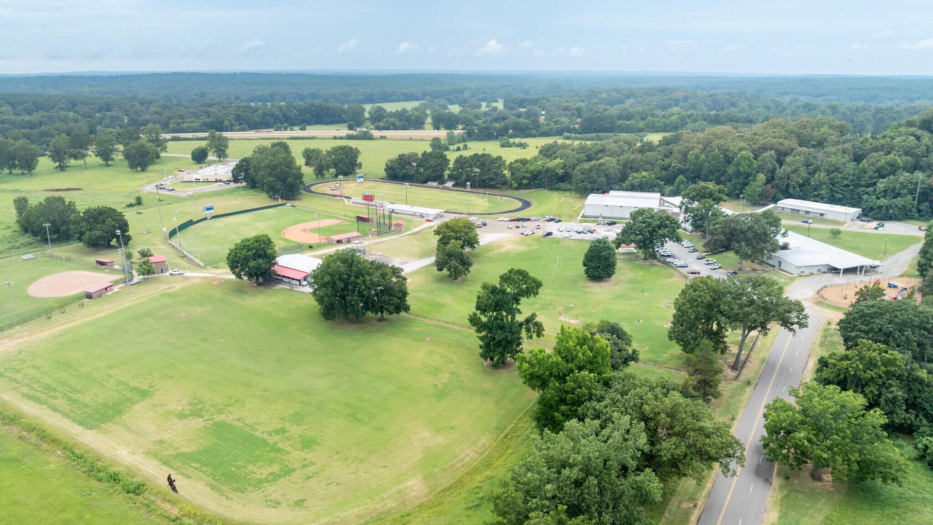 Aerial view of a lush green park with sporting fields, trees, and a gravel road.