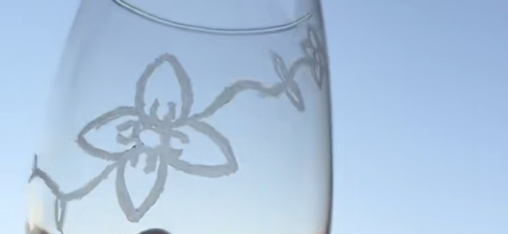 A hand holding a frosted glass featuring a floral design against a blue sky.