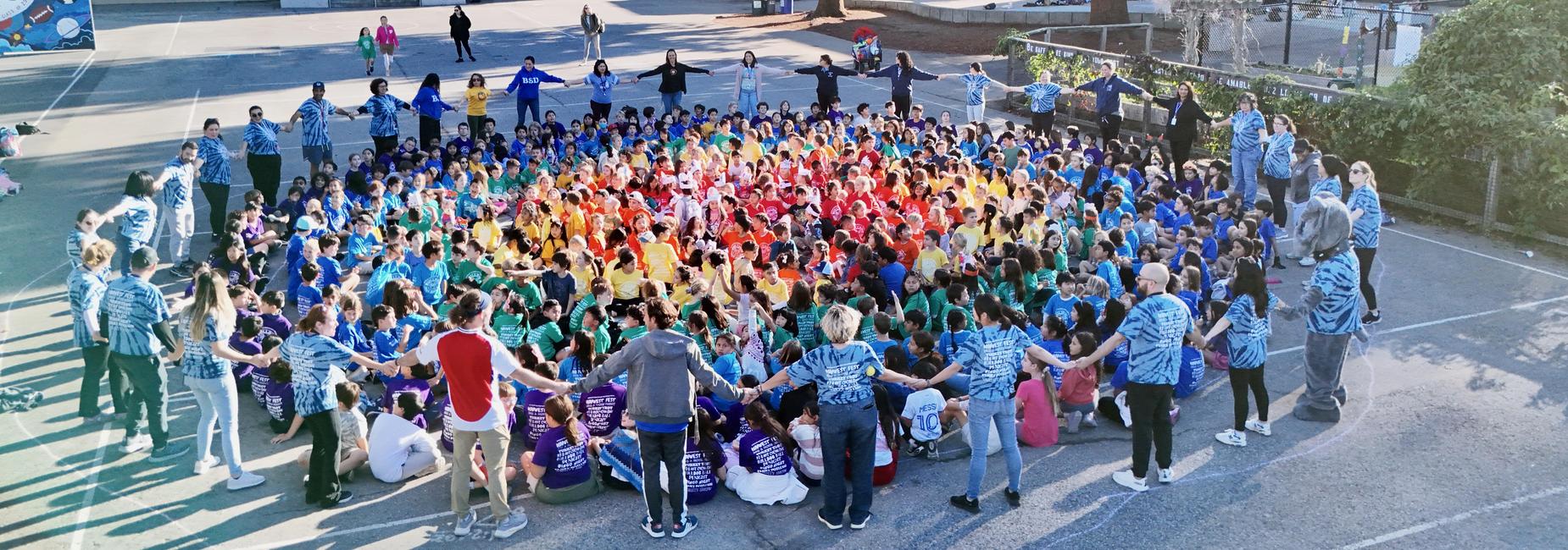McKinley school in rainbow shirts forming a circle outdoors, holding hands.