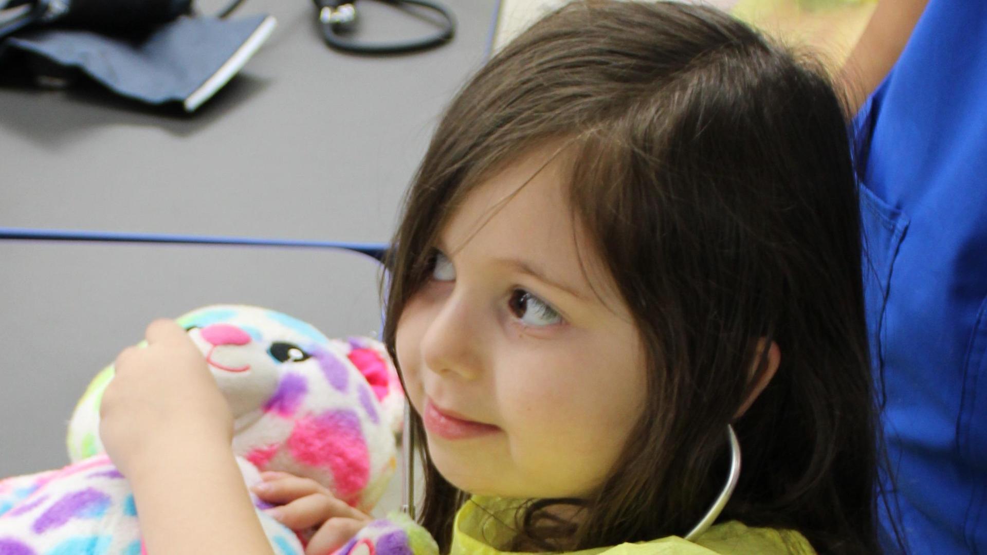 Child holding a colorful stuffed animal with a joyful expression.