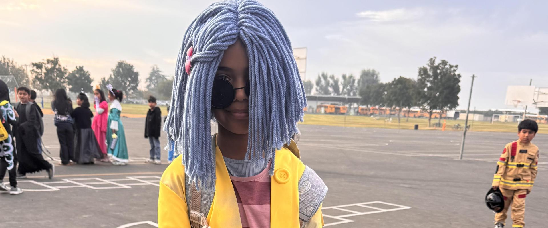 Child in a yellow coat with a striped shirt and light blue hair.
