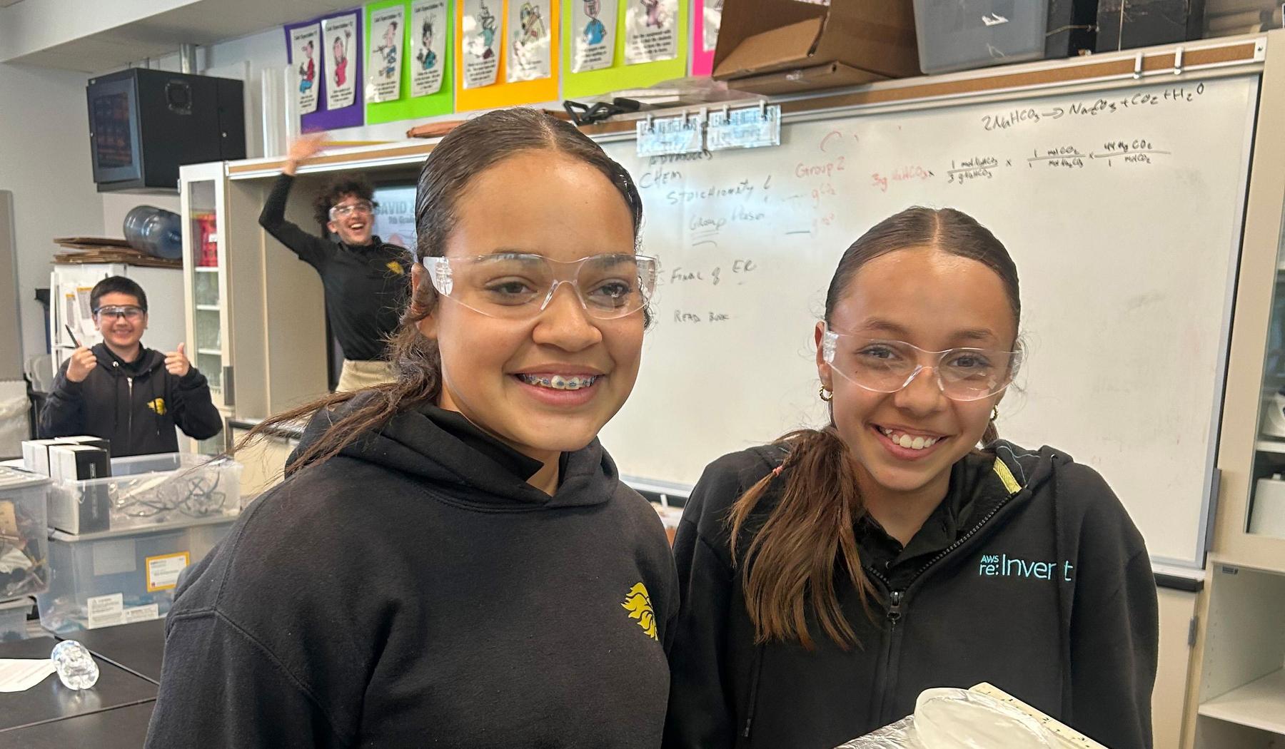 two girls in science class with boys being silly in the background