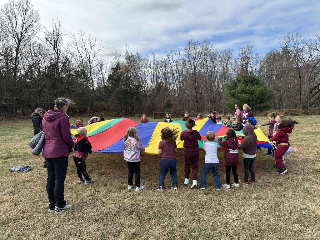 Elementary students holding up a round, multicolored parachute outside.