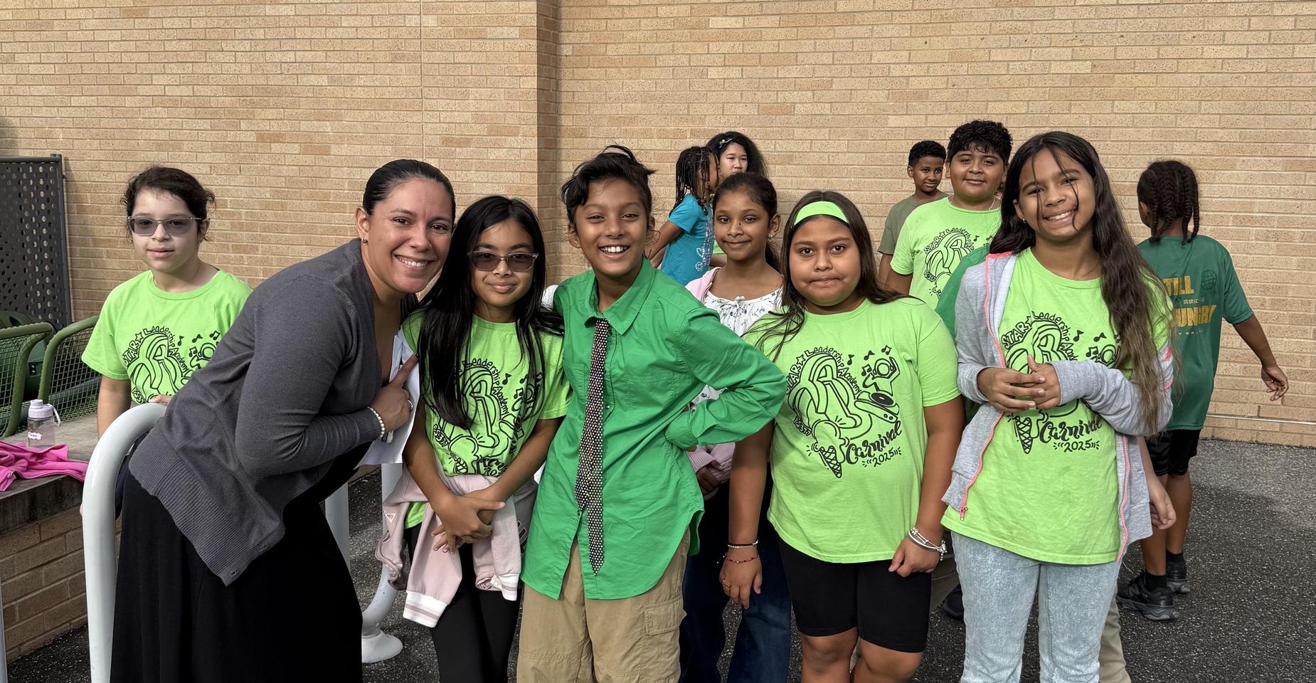Group of children in green shirts with an adult, smiling outdoors.