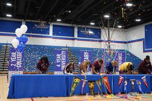 Students sign commitment letters with confetti and banners in a gymnasium.