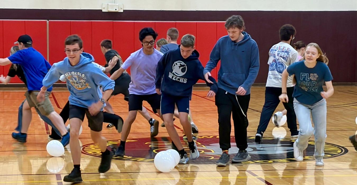 Students participating in a gym activity, running with balloons.