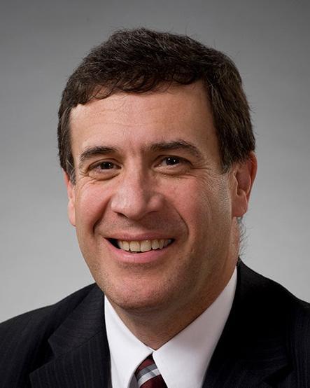 smiling white man with dark brown hair in a black suit jacket with a white shirt