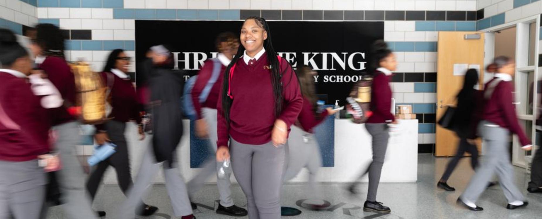 Students in uniforms walking through a school hallway with a large sign.