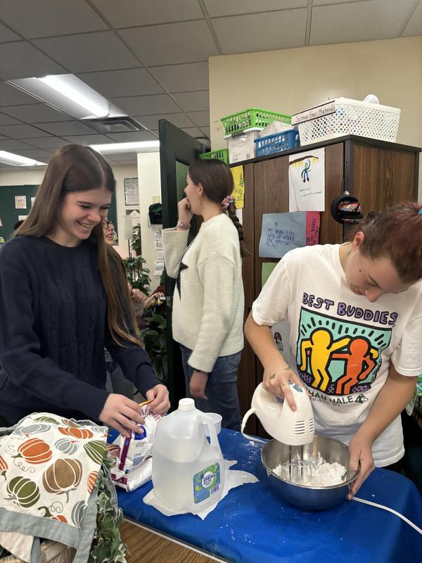 Students preparing a mixture with a mixer in a classroom setting.