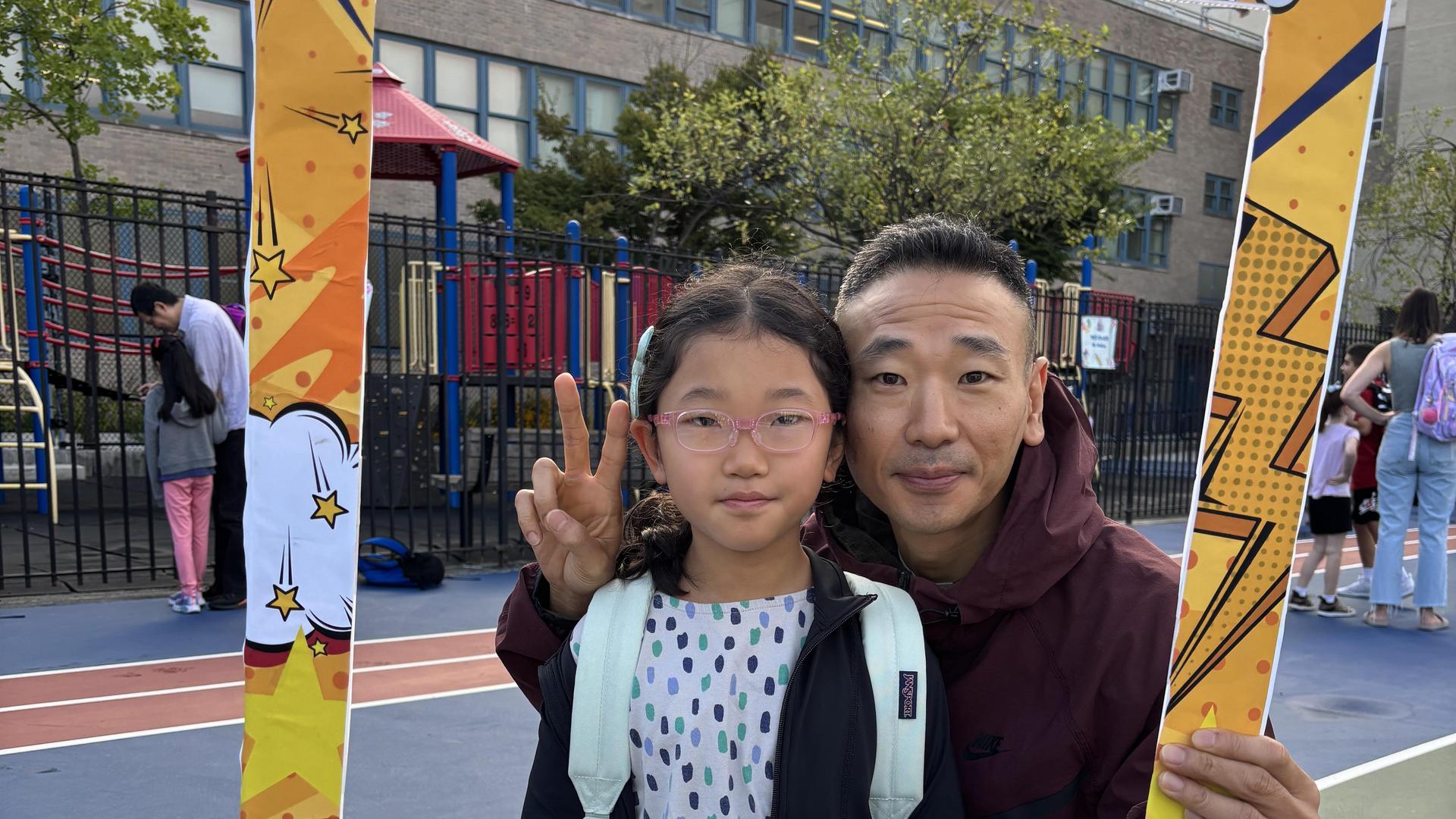 Child with glasses and adult man holding a photo frame at a school event.