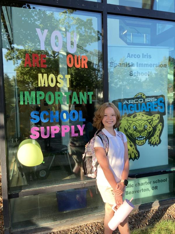 An Arco Iris student stands in front of a glass window that displays the message, “You are our most important school supply.”
