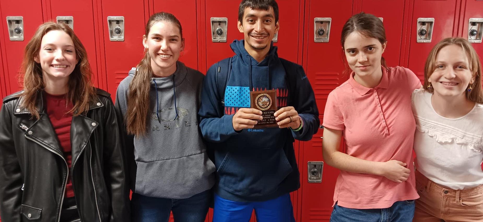Five students standing in front of red lockers, one holding a plaque.