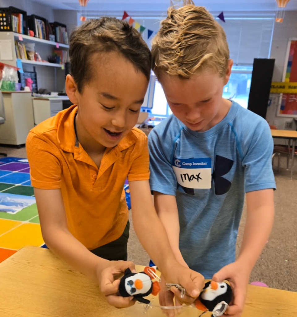 Two boys joyfully holding stuffed puffins in a classroom.