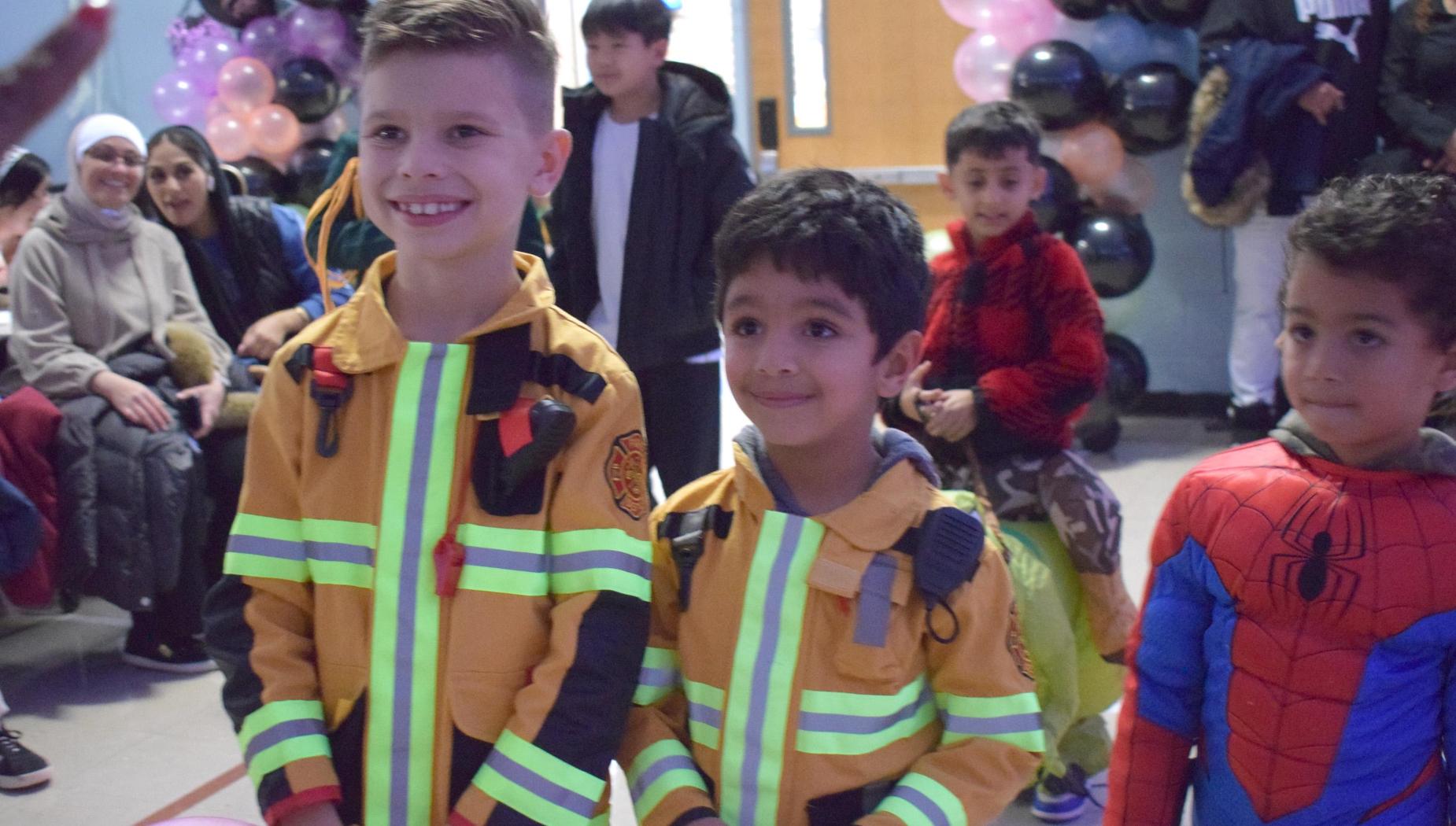 Two boys in firefighter costumes smile at the camera during a celebration.