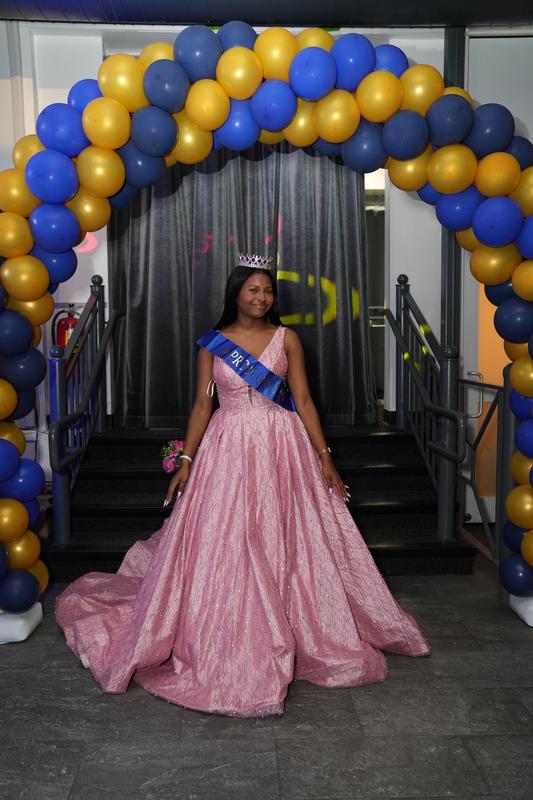 A person in a pink gown poses under a balloon arch.