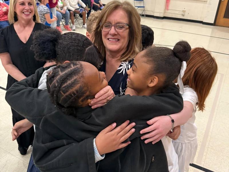 A joyful group hug among children and an adult in a classroom setting.