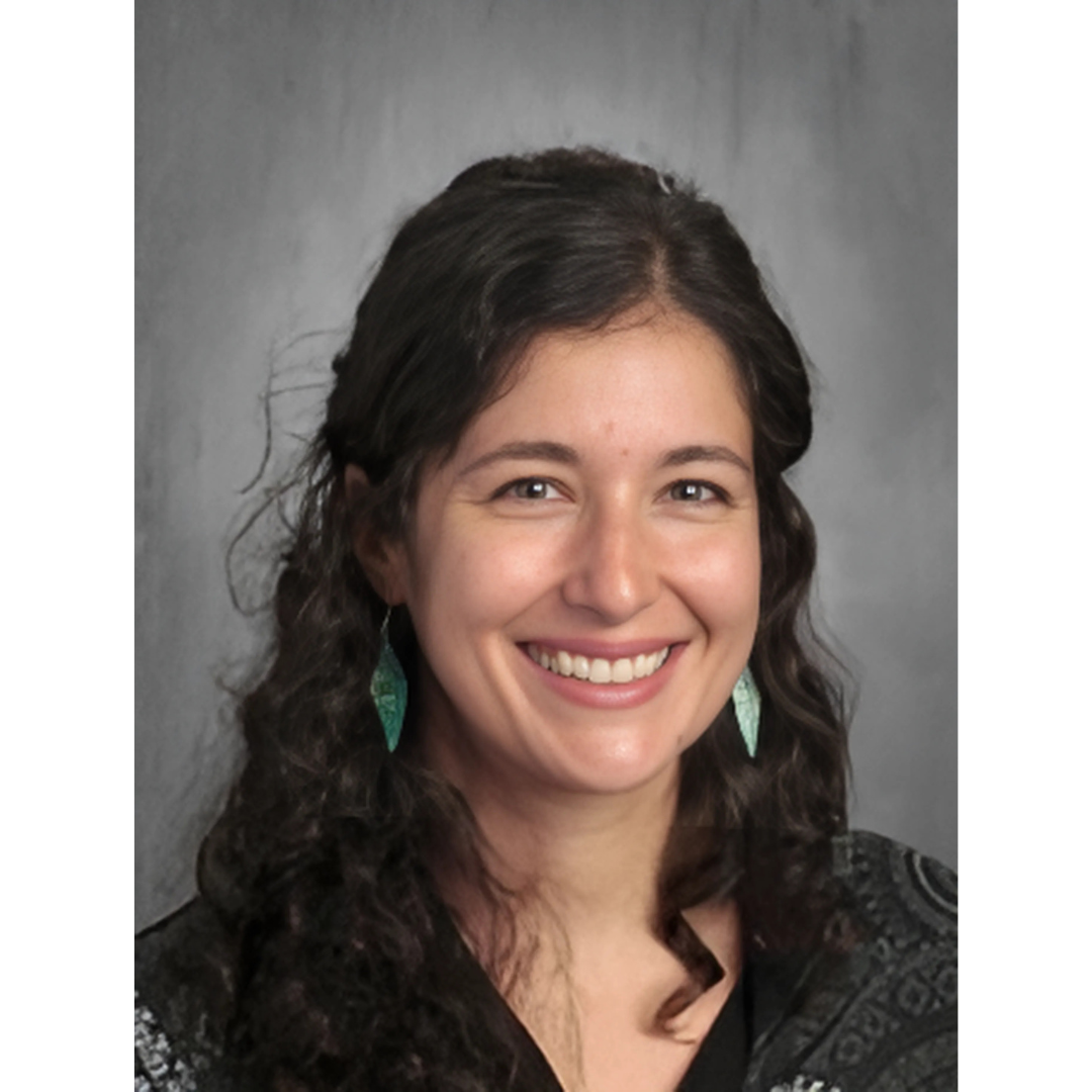 a person with curly hair and green earrings smiling