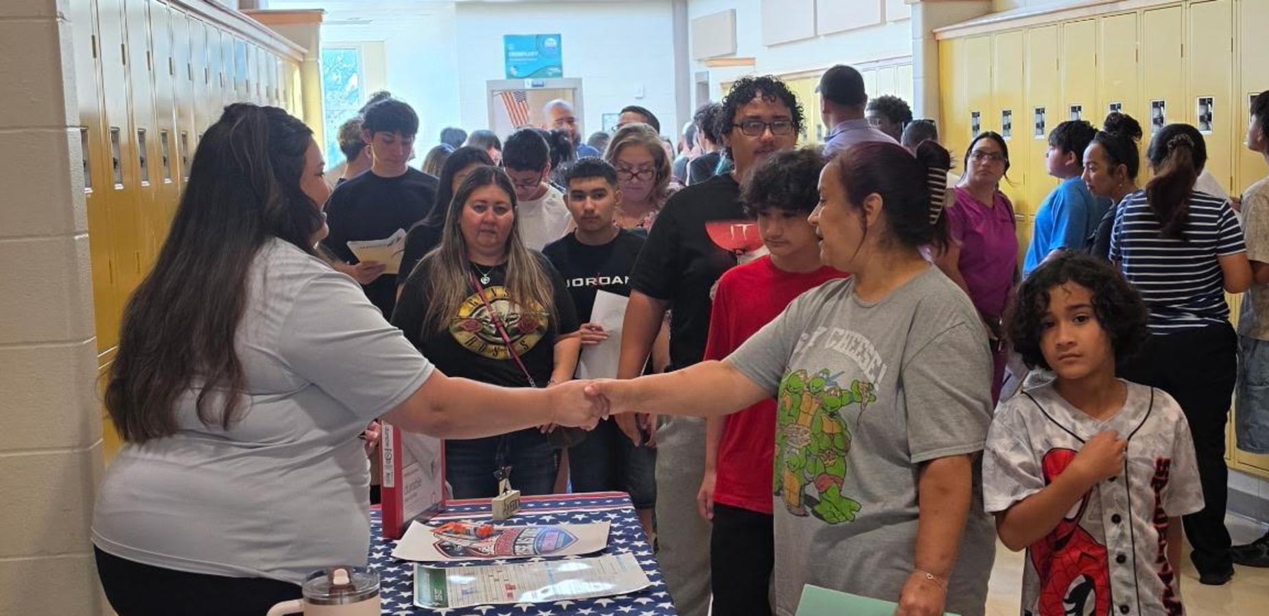 A busy school hallway filled with people, some shaking hands and engaging.