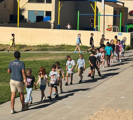 students walking in a line following an adult who is walking backwards facing the students