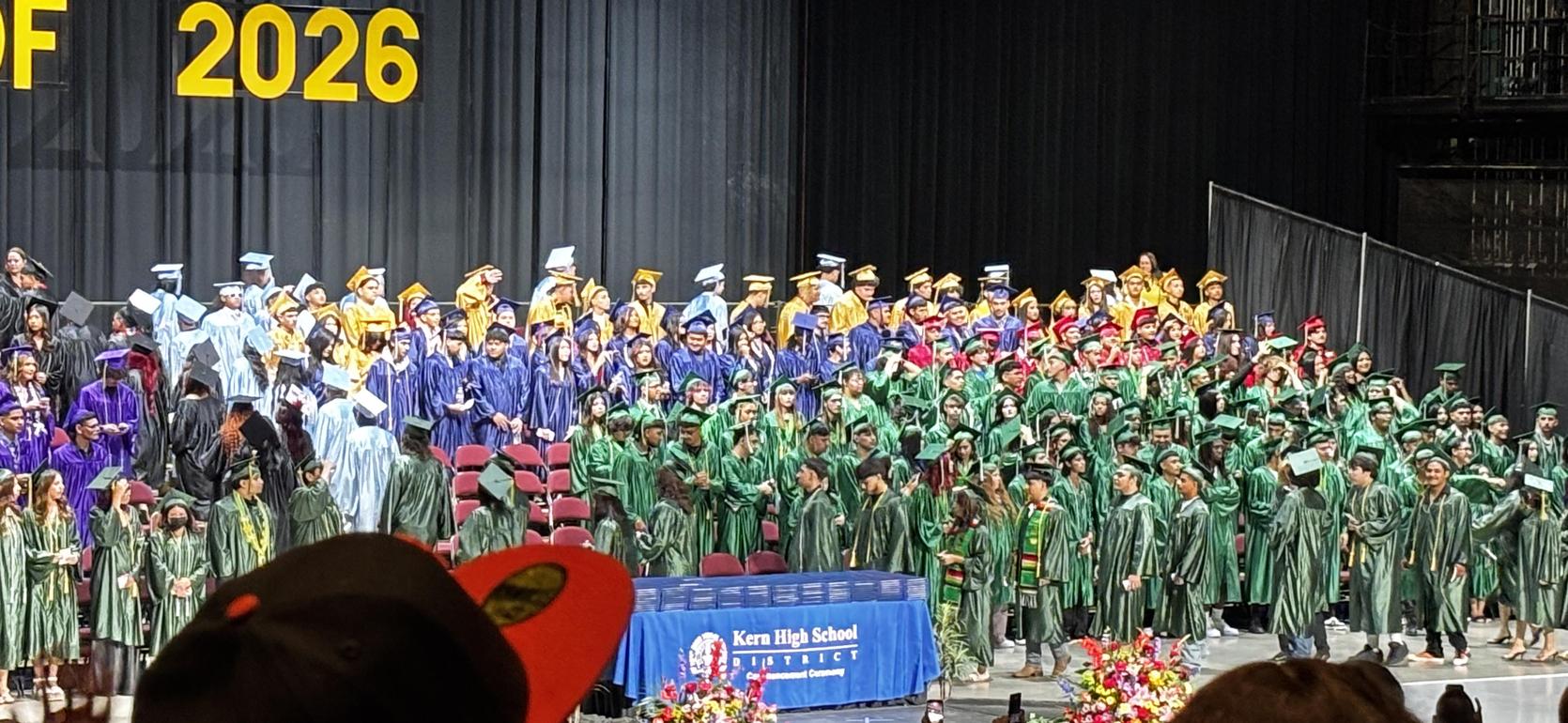 Large group of graduates in colorful gowns standing together during a graduation ceremony.