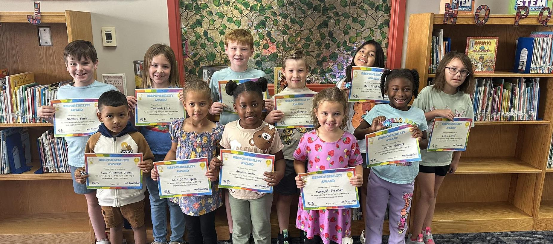 Group of students standing in the library holding certificates