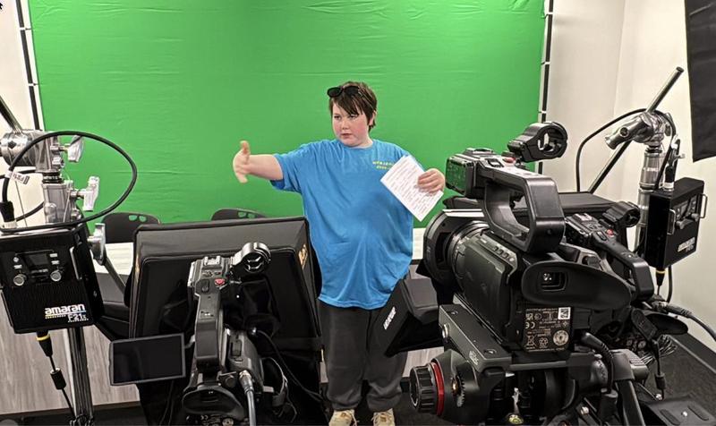 Middle school boy gestures at broadcasting equipment