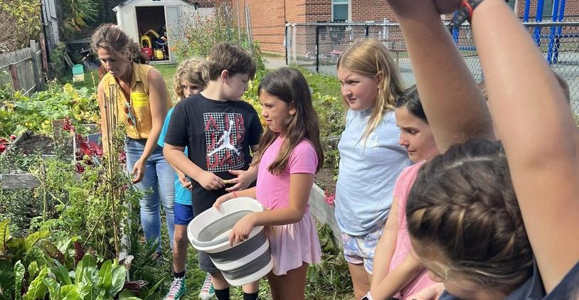 Children participating in a garden activity with a teacher nearby.