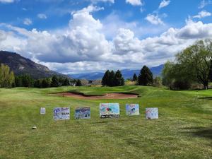 Five signs in front of a golf-course green that feature student-created drawings