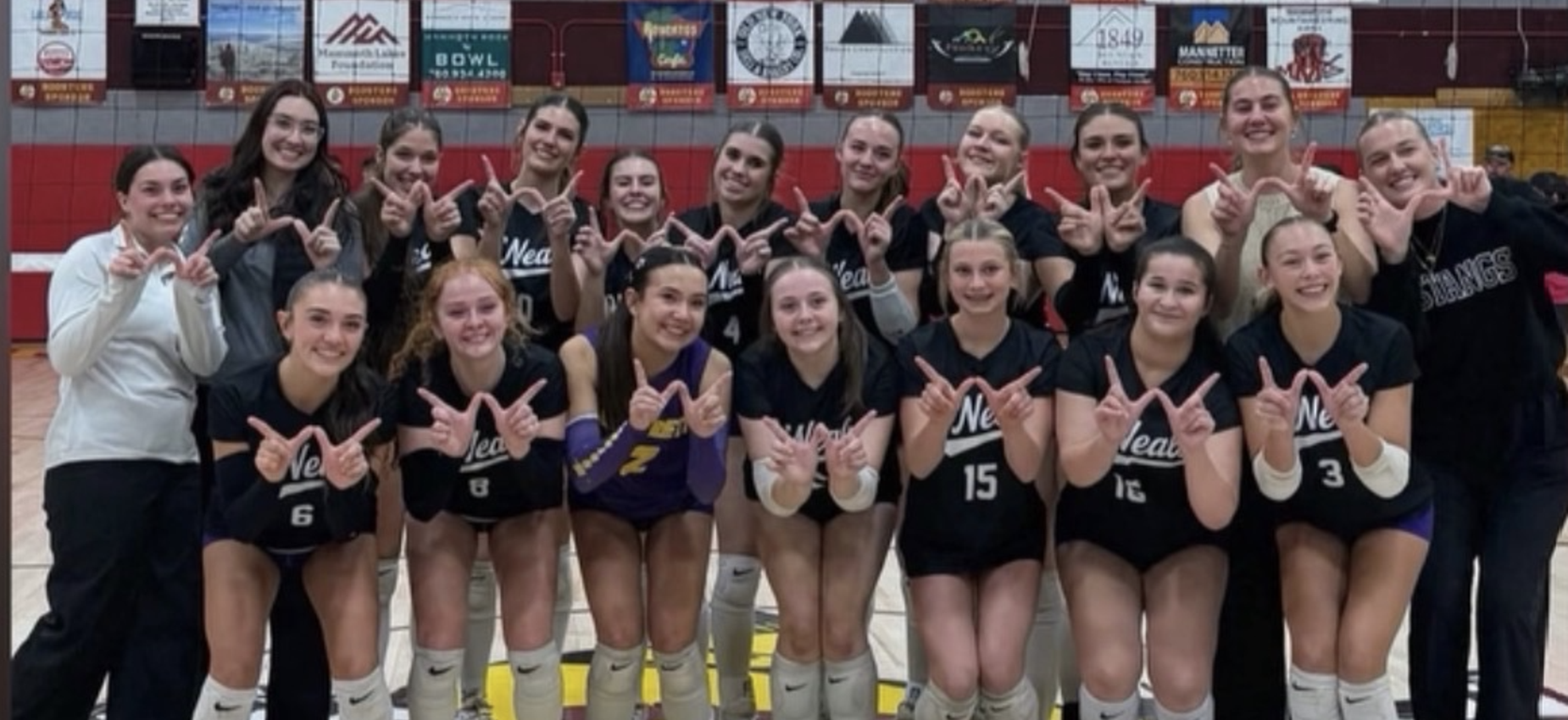 A volleyball team posing together in a gym, making 'W' signs with their hands.
