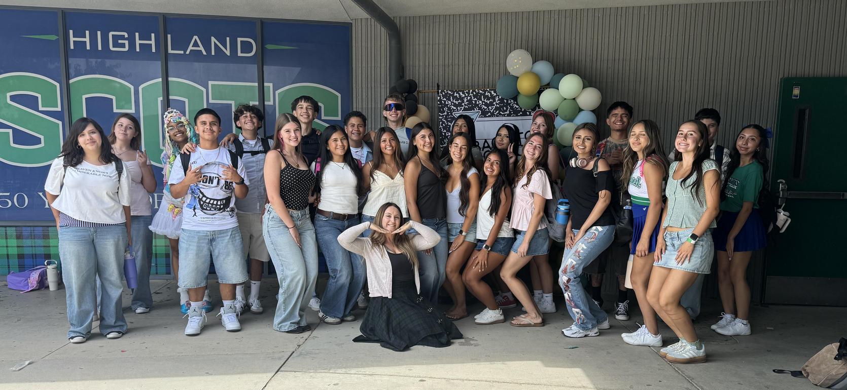 Group of people posing together outdoors with decorations and a school backdrop.