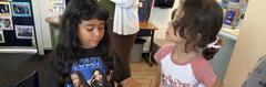 Two young girls interacting in a classroom setting.
