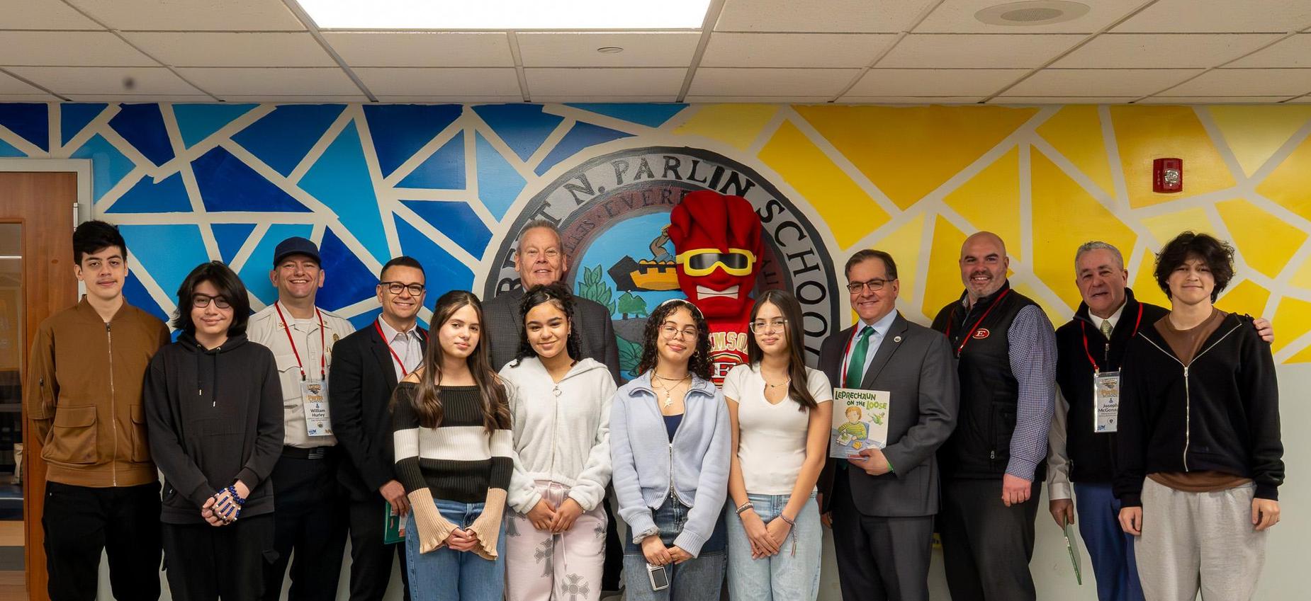 Group of students and adults posing in a brightly painted school hallway.