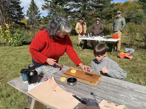 An adult assists a child with a project at a table outdoors.