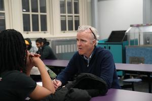 A man and a student engaging in a discussion at a table in a study space.