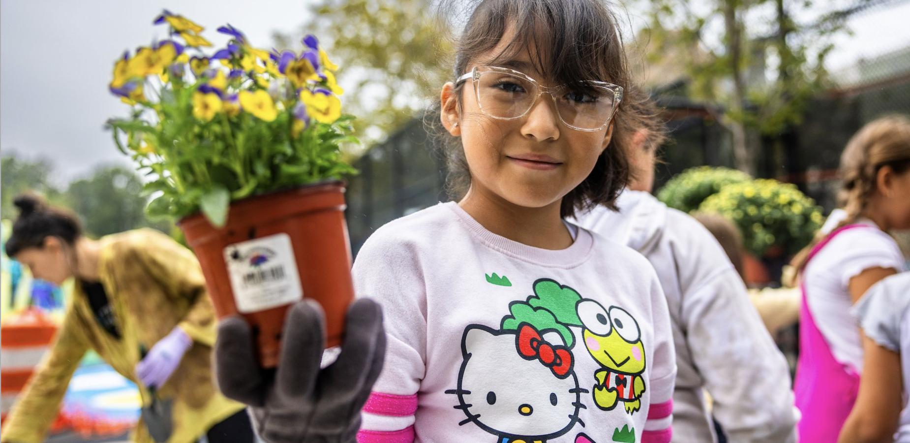 Young girl holding a potted plant, wearing glasses and a colorful shirt.