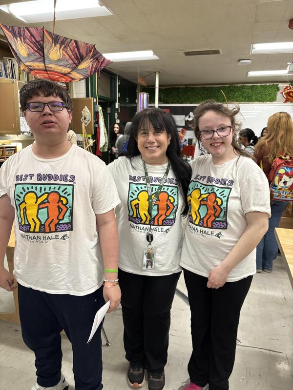 Three individuals wearing 'Best Buddies' shirts posing together with smiles.