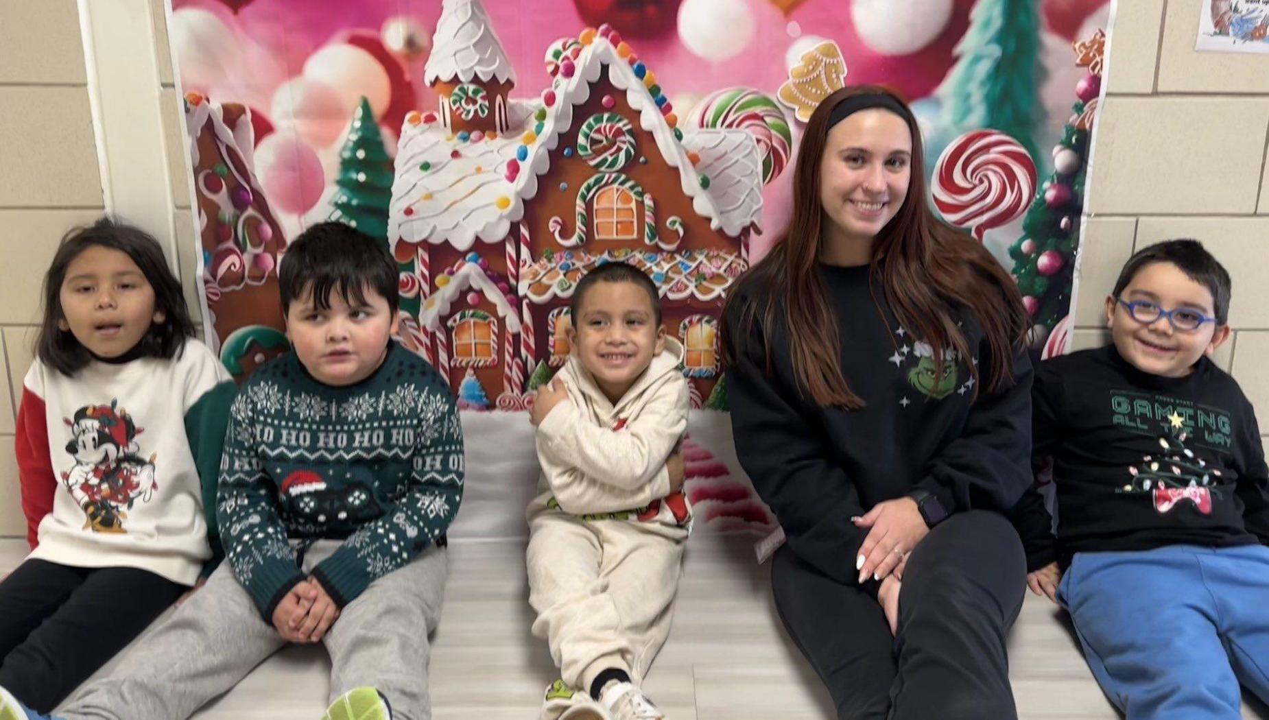 Five children and an adult pose happily in front of a gingerbread-themed backdrop.