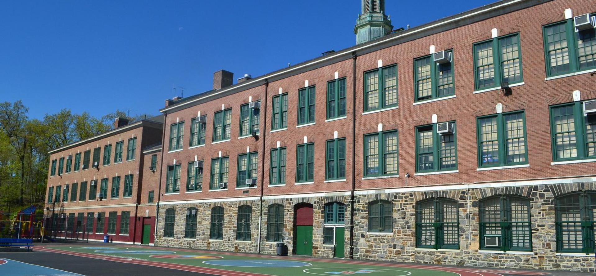 Brick school structure showcasing multiple green windows and a playground area.