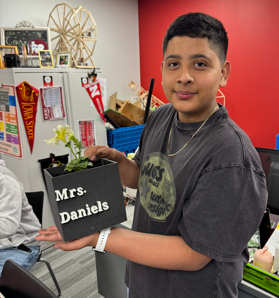 Boy holding a planter labeled 'Mrs. Daniels' with a flower inside.