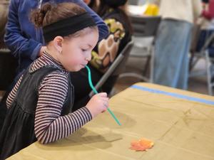 A student uses a straw to blow a leaf at the STEAM station