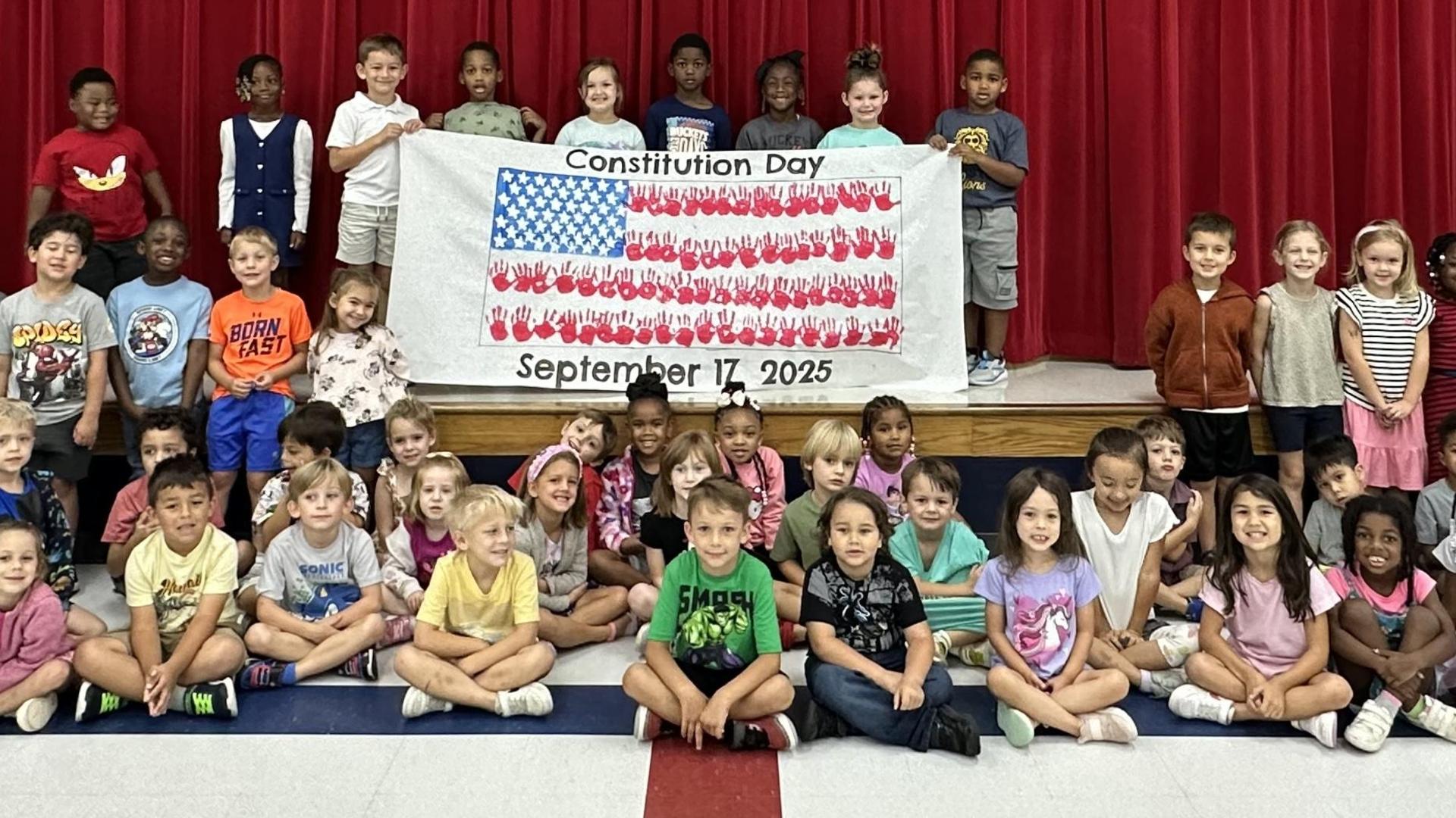 A diverse group of children posing together with a Constitution Day banner.