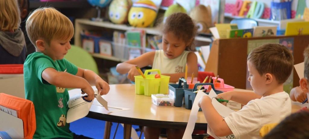 Three students cutting paper with scissors.