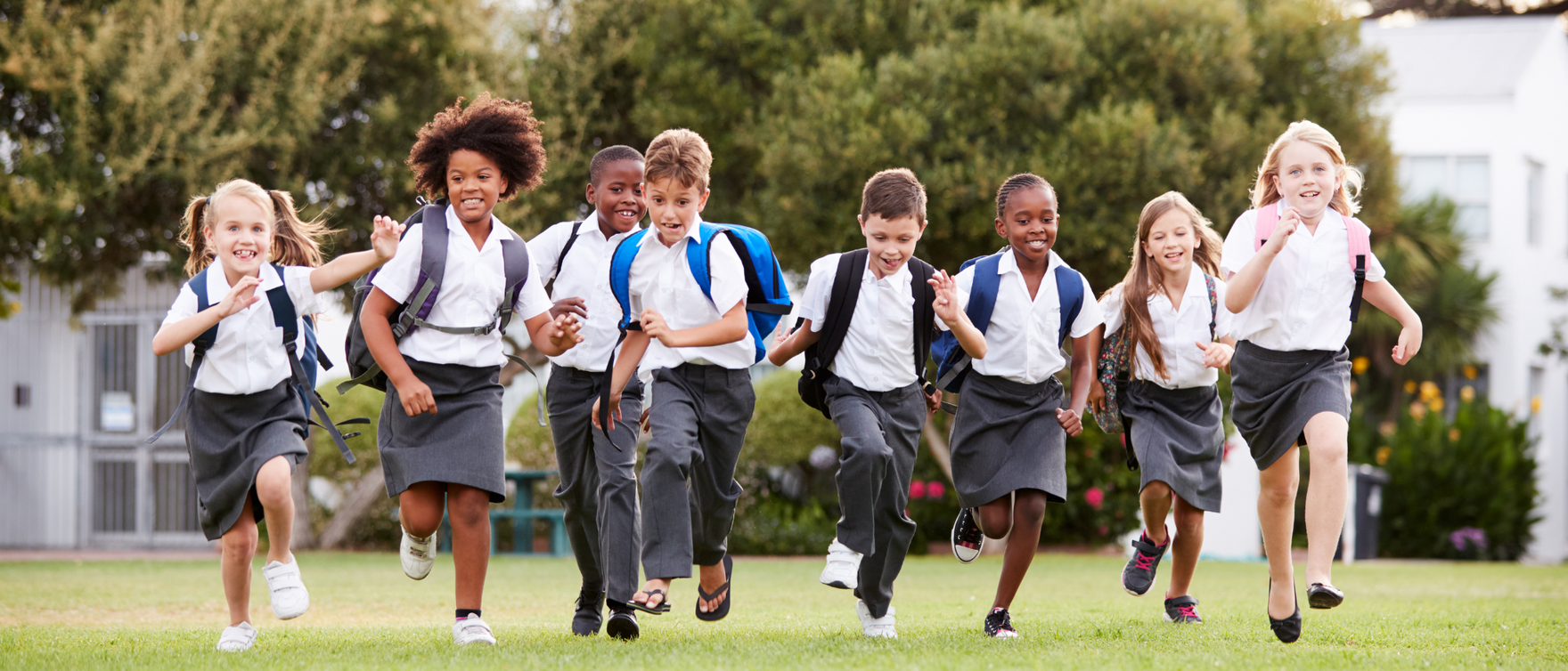 Group of children running together in school uniforms on a grassy field.