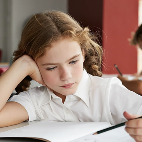 Concentrated girl with curly hair working on a drawing at a desk.