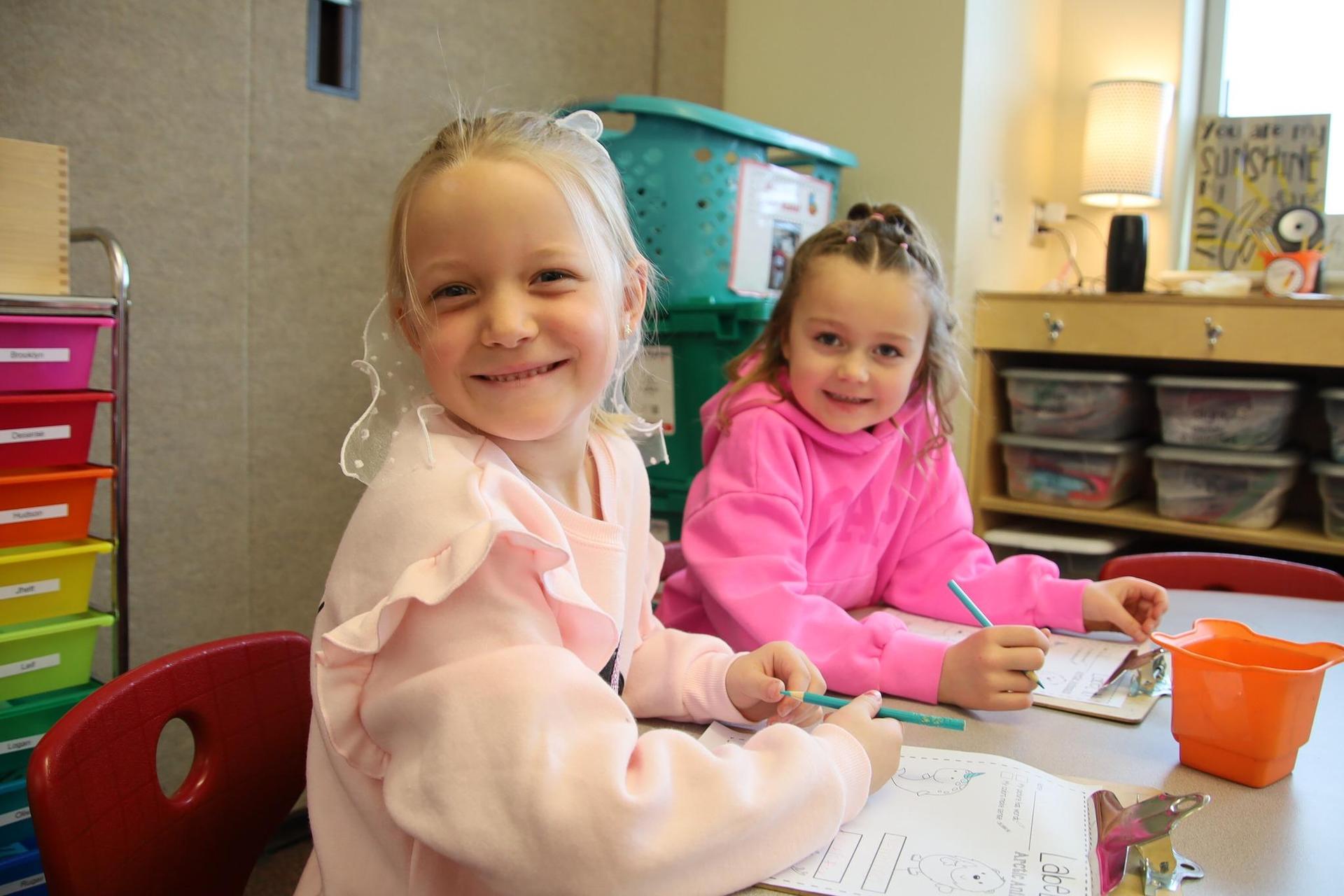 elementary school girls smiling for the camera in a classroom