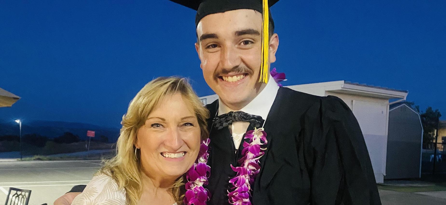 Man in graduation attire with a floral lei posing with a smiling woman.