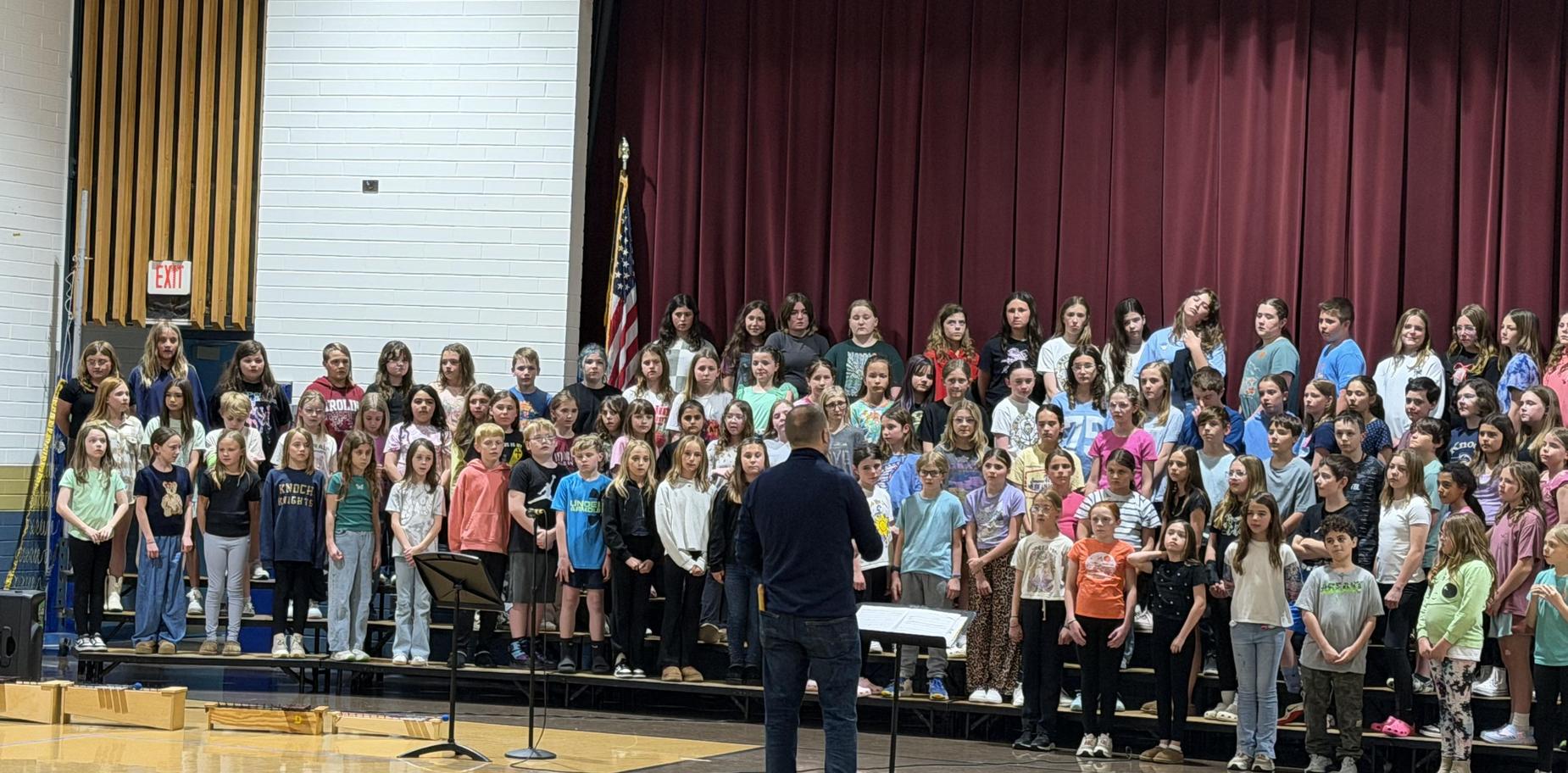 Students performing on stage with a choir director in a school auditorium.
