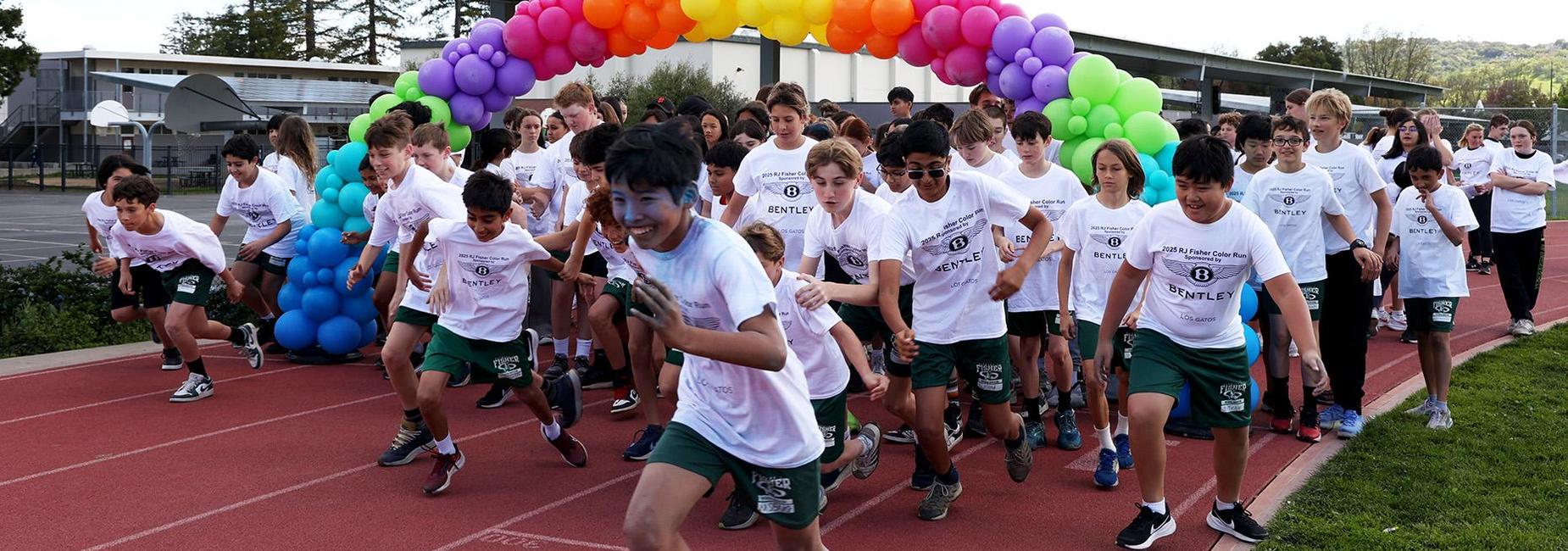 students running under a colorful balloon arch on track