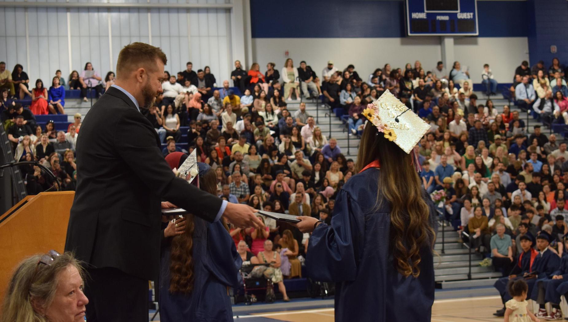 A graduate receiving a diploma from a man on stage, with a crowd in the background.